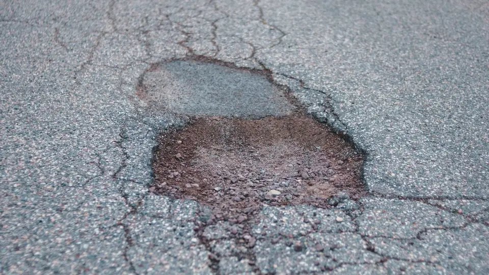 Pothole and raveled asphalt showing loose aggregate at the broken edge